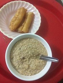 Thick, brown, medium textured porridge in bowl next to plate of fried tofu.