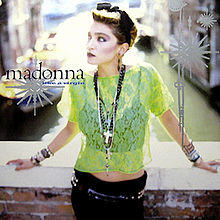 Madonna standing on a bridge wearing a light green see-through top, a bridal mini-veil and black pants.