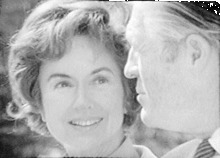 Black-and-white image of Lenore Romney in full face smiling at George Romney in profile
