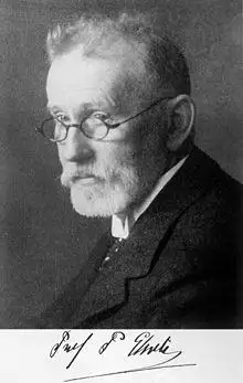 Portrait of an older, thin man with a beard wearing glasses and dressed in a suit and tie