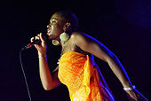 A woman wearing an orange dress while singing into a microphone.