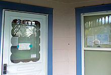 Outer door and window of a house with several paper notices taped to both of them