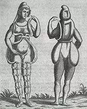 A front and back illustration of a Renaissance-era hermaphrodite showing a person with female facial features, breasts, and what appears to be a small penis or large clitoris. She wears a small hood and open robe tied multiple times around the legs. Where it opens in the front, the apparent rear appearance shows it to be perhaps a shell of some kind, as one with her body Two squares are missing from her the back of her head and torso. She has no buttocks.