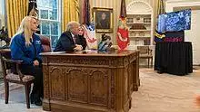 Donald Trump sitting behind the desk with a large screen infront of it
