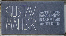 A dark plaque with white lettering in which the composer's name is shown in extra large characters on the left, the main message in smaller characters on the right