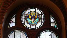 A half dark blue, half light blue circle with the words Collegium Georgiopolitanum 1789 inscribed around the edge in gold with a gold federal eagle in the center holding a cross and a globe in its talons, and a scroll with the motto Utraque Unum in its beak. Sixteen gold stars are arranged around the eagle, and a gold instrument above it.
