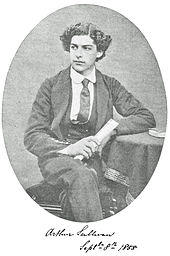 Sullivan seated with one leg crossed over another, age 16, in his Royal Academy of Music uniform, showing his thick, curly hair. Black and white.
