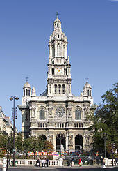 A 19th-century church in the French style, in light coloured stone, with a central tower with rounded top and smaller towers set back to left and right.
