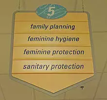 A yellow sign with a pointed bottom. At the top is the number 5 in an oval with a blue background. Below it are the words "family planning", "feminine hygiene", "feminine protection" and "sanitary protection"