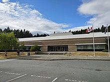 Colour photo of Francis Kelsey Seconday School, a single-storey brick school surrounded by trees, with flagpoles flying the flags for Canada and for British Columbia