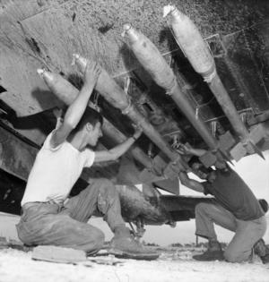 Five-inch rockets being loaded under the wing of an F4U of MAG-33. - NARA - 532561 - restored.png