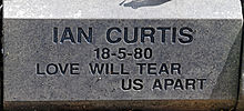 A grey stone with "Ian Curtis, 18-5-80, Love Will Tear Us Apart" carved into it in block letters