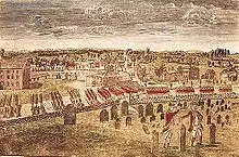 A birds-eye view of a long column of British soldiers marching by regiment along a road just outside of Boston