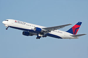 A side/underneath view of a Boeing 767-300 in Delta Air Lines' white, blue and red color during climbout. The main undercarriage doors are retracting.