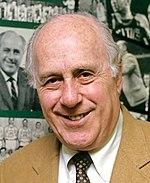 A man looking ahead. He is wearing a jacket and tie.