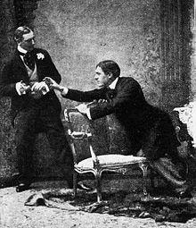 Young man in Victorian clothes reaching toward a cigarette case held by another similarly attired young man