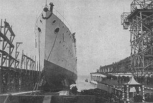 a ship is launched into the ocean in the middle of a construction yard, with a large crowd celebrating the occasion.
