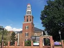 An 18th-century red brick church with white steeple behind a modern road in autumn.