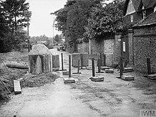 A series of concrete blocks and upright steel girders, block the road from use by vehicles.
