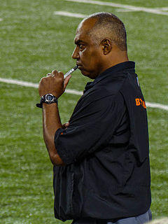 Color photograph of man (Marvin Lewis) wearing black sport shirt, standing on football sideline and holding a capped Sharpie marker to his lips.