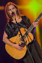 A young brunette woman in a blue dress behind a keyboard and microphone.