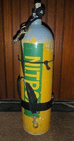 The sling harness is shown on a standing cylinder, with the bolt snaps for chest and hip connection and the connecting webbing and a cambelt securing the lower end of the webbing strap to the body of the cylinder.