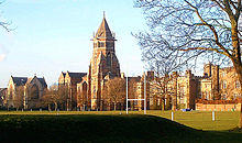 A wide shot of an old English school with a central tower, with a sports pitch in the foreground.