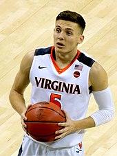 A college basketball player dressed in white with orange and blue bordering prepares to shoot a free throw.